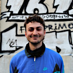 Foto von Veit Joneleit vor einer Graffiti-Wand. Auf dieser steht unter anderem: ANTIFA